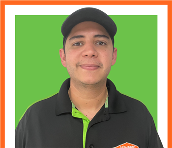 Luis Bruzual Garcia, SERVPRO employee in uniform in front of green SERVPRO logo