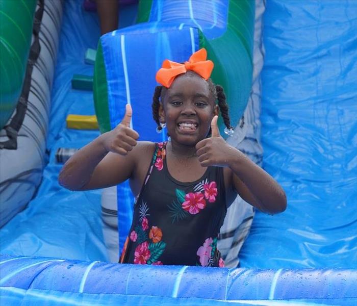 girl at bottom of blue slide smiling with thumbs up