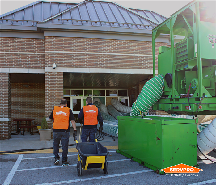 Two SERVPRO of Bartlett / Cordova crew in orange vests walking into a school next to a big, green desiccant dehumidifier 